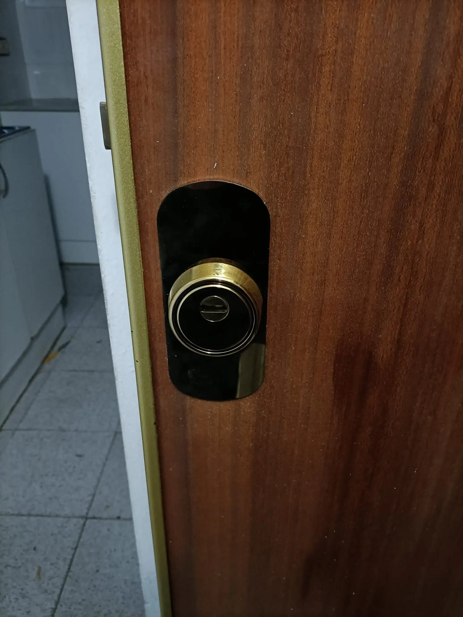 Cambio de cerradura con escudo de seguridad dorado y negro instalado en puerta de madera marrón
