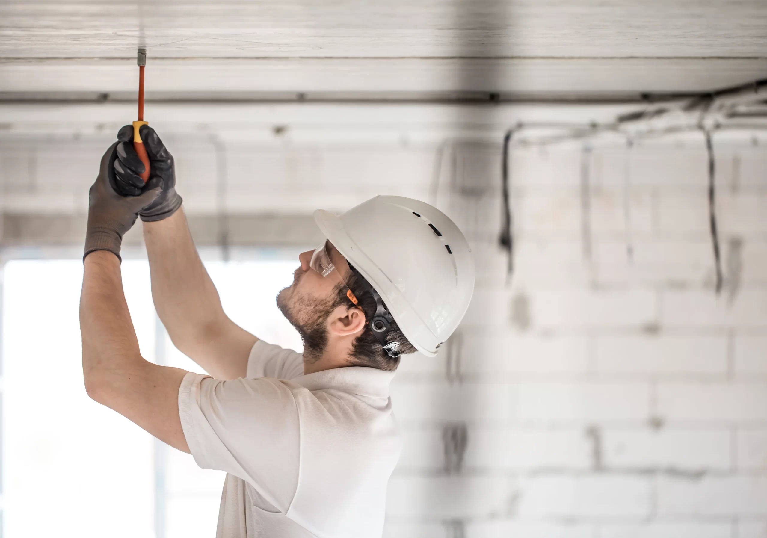 Técnico instalador con casco de seguridad reparando el anclaje del motor de una puerta de garaje automática